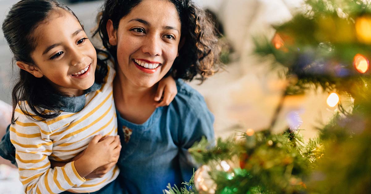 Mother hugging daughter next to Christmas tree