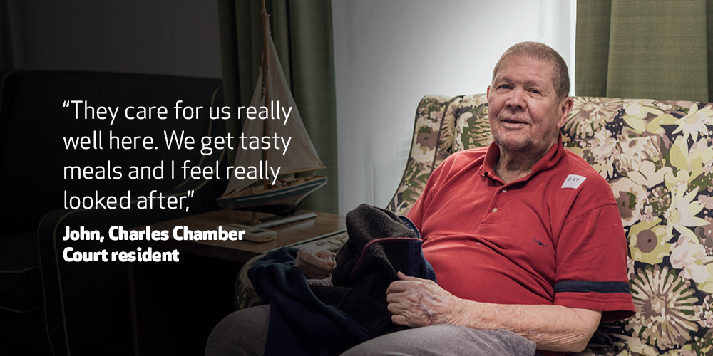 Elderly man smiling and looking toward the camera. “They care for us really well here. We get tasty meals and I feel really looked after,” – John, Charles Chamber Court resident 