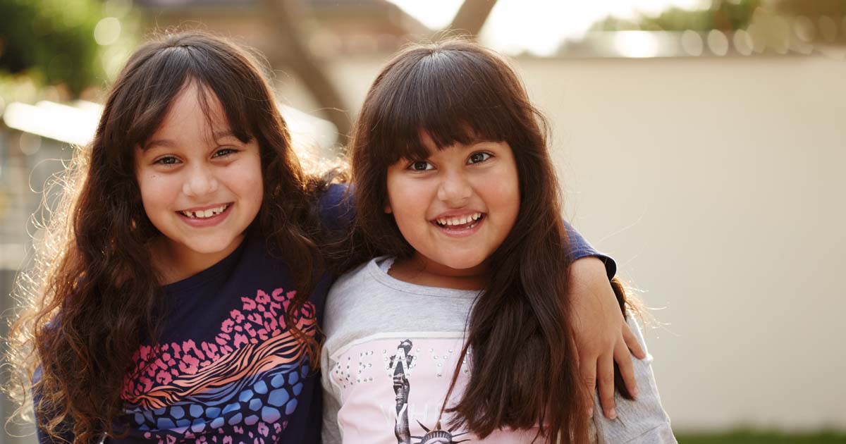 Two smiling young sisters standing outside