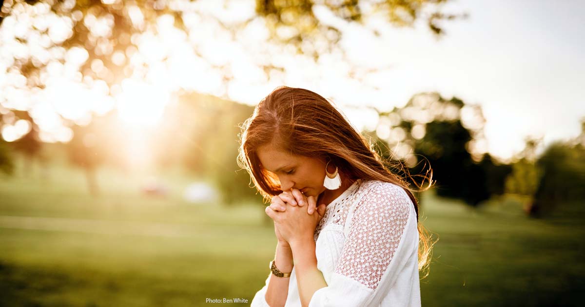 Young woman with her head resting on clasped hands, outside in the sun, deep in thought.