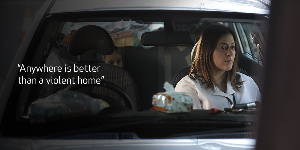 Woman in car and her daughter is in the back seat. Text reads “Anywhere is better than a violent home.”