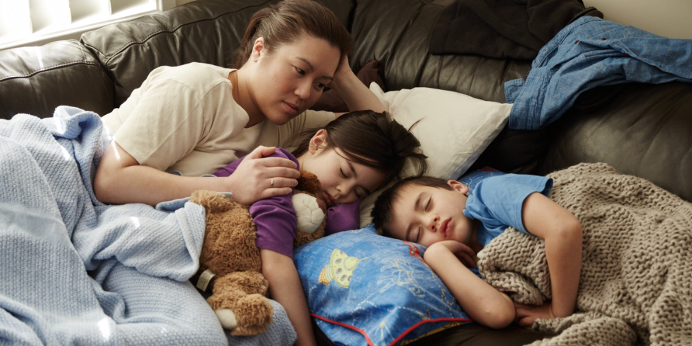 A worried Jenny lies on the couch next to her two children with a concerned look on her face. 