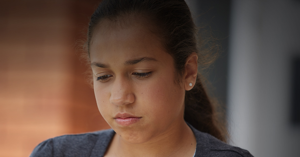 Young girl standing next to a wall looking sad