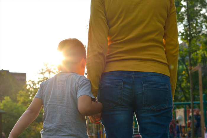 Mother and young child hold hands outdoors.