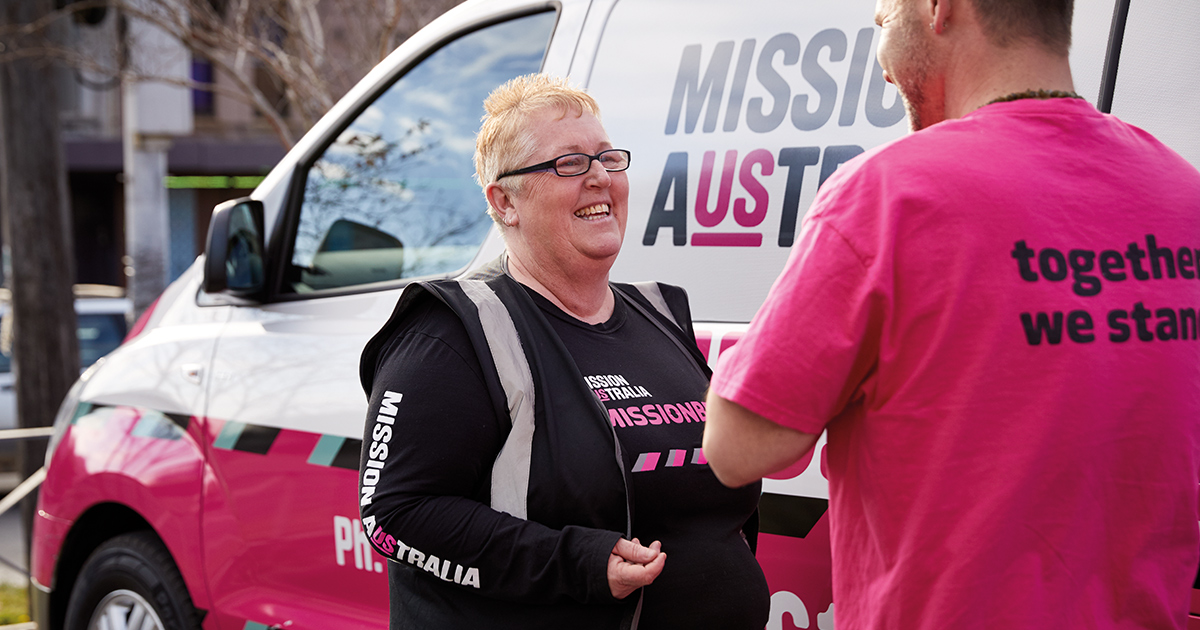 Two people talking next to a Missionbeat van