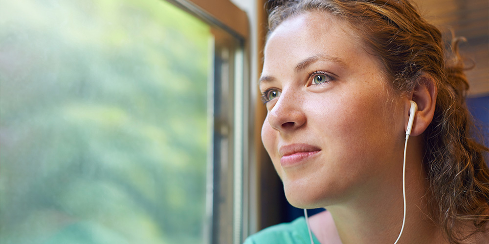 Young woman smiling, listening to music and looking out the window.  