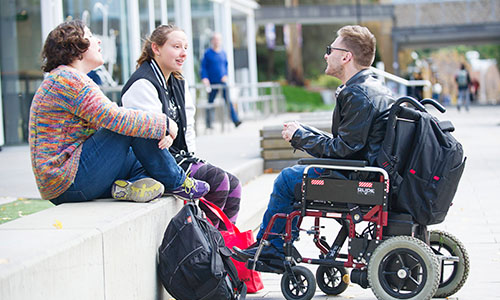 3 people talking, 2 sitting on a platform and 1 in a wheelchair